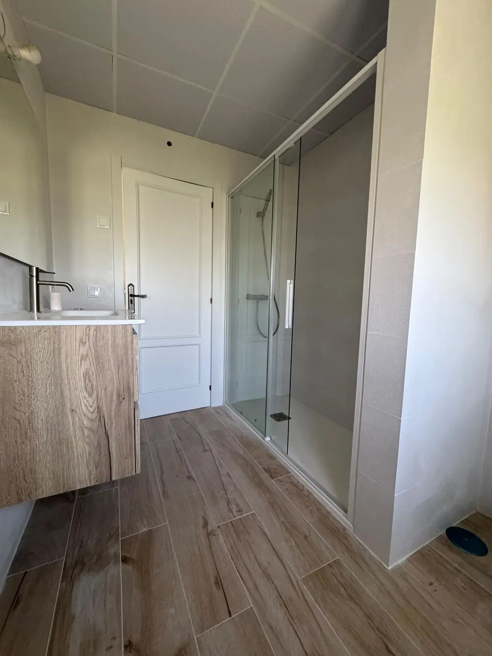 Baño reformado con plato de ducha y mampara, mueble de madera y suelo efecto madera