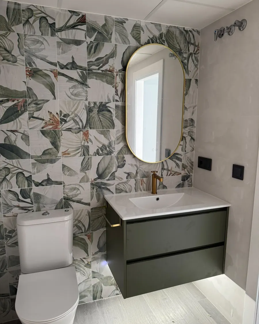 Baño alicatado con azulejo de hojas tropicales y mueble verde