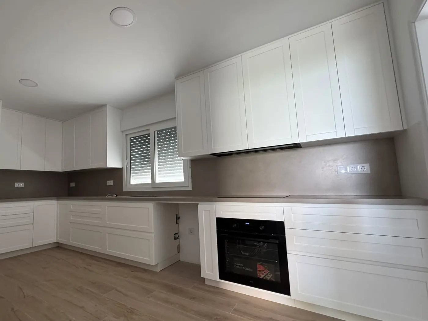 Cocina reformada en L con muebles blancos, encimera gris y suelo efecto madera