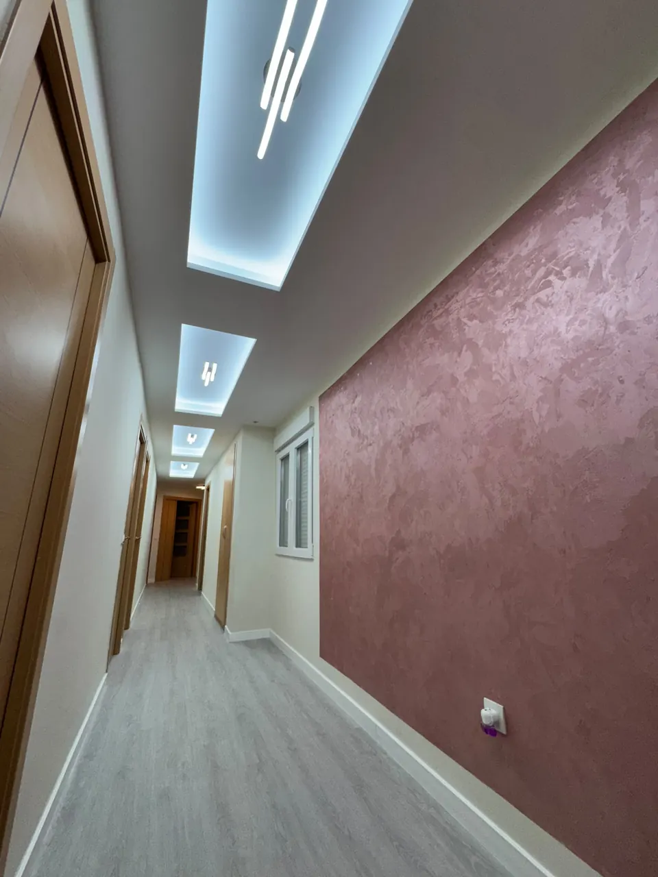 Pasillo después de la reforma: techo nuevo con iluminación LED, pared de estuco rosa y suelo nuevo